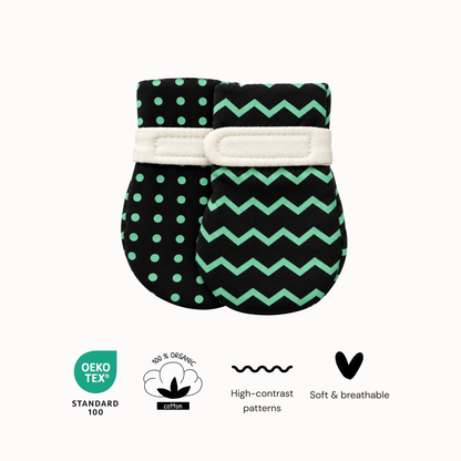 Two high-contrast baby mittens with visual patterns, one with green polka dots and the other with a green chevron, featuring a white elastic band. Below the products are four circular and text badges indicating Oeko Tex Standard 100, 100% Organic Cotton, high-contrast patterns, and soft & breathable material.